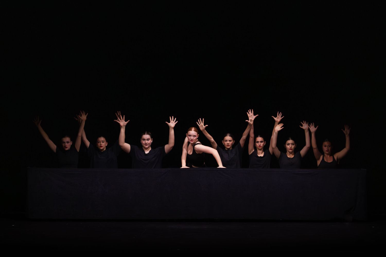 Silhouetted performers with raised arms pose dramatically against a dark background on stage.