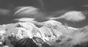 Black and white panorama of snow-covered mountain peaks with dramatic clouds.