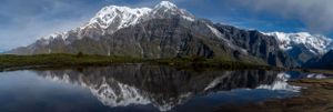 Panoramic view of snow-capped mountains reflected in a pristine alpine lake.