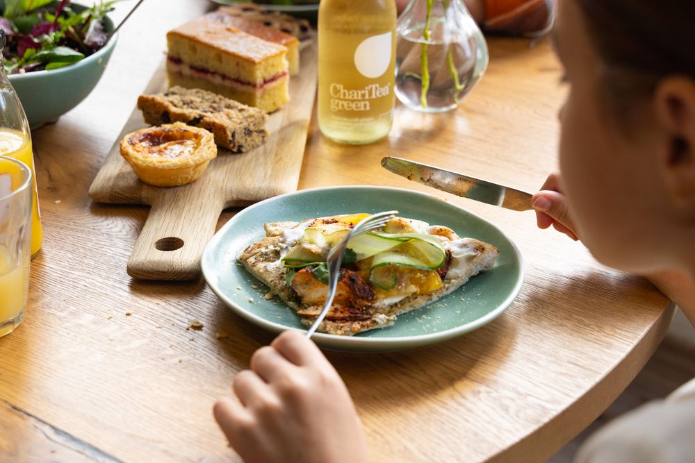 A plate of eggs benedict with hollandaise sauce sits on a wooden table next to bread and drinks during brunch.