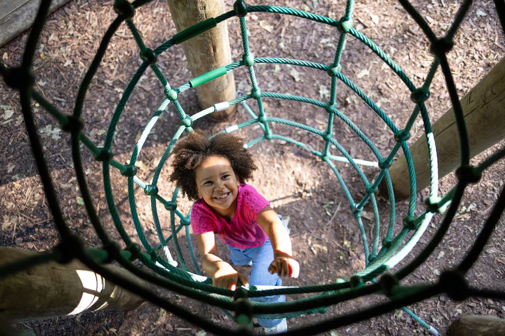 Overhead view looking down a spiral turquoise climbing structure at a playground on a sunny day.