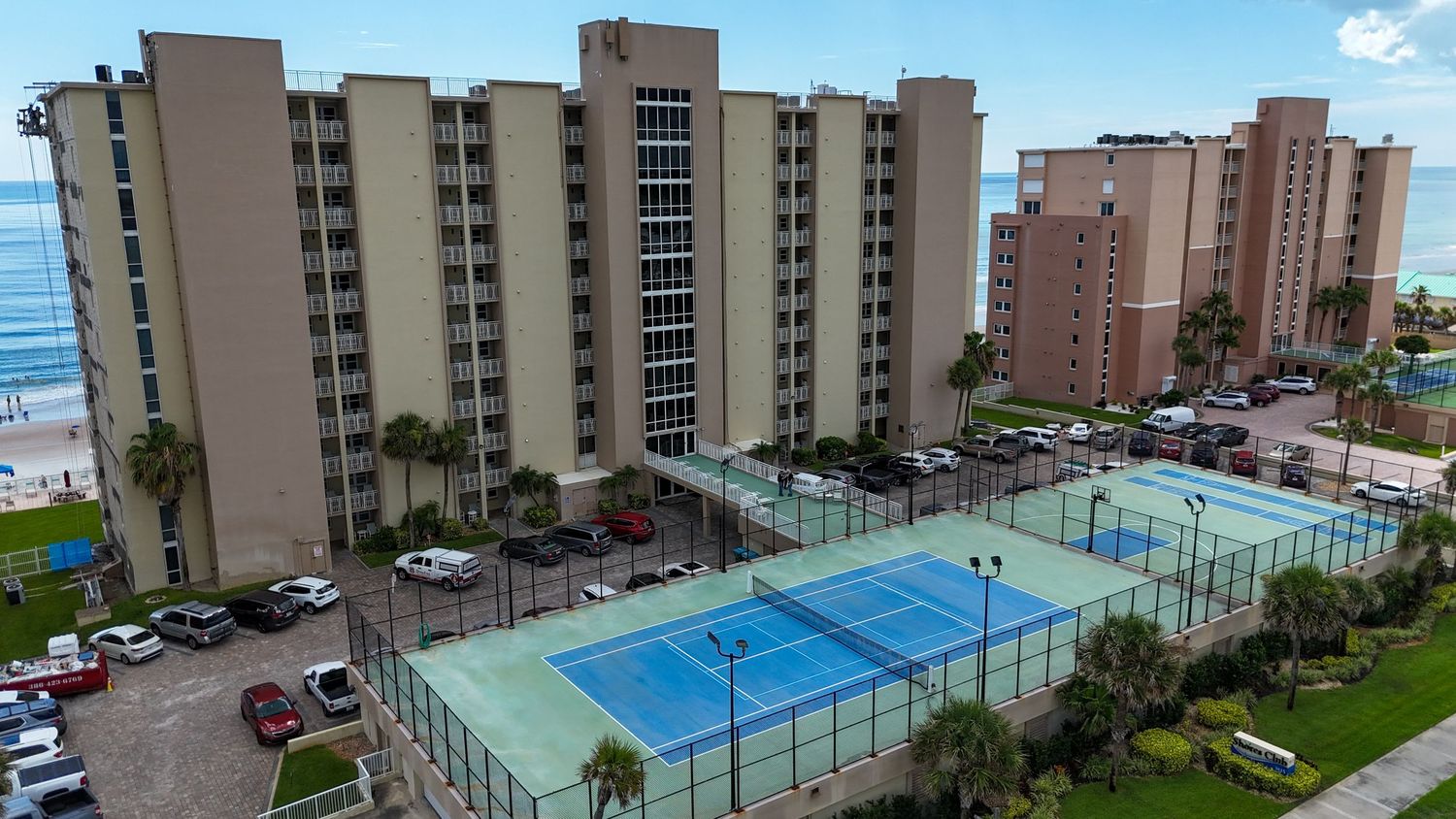 Aerial view of beige high-rise condominiums with tennis courts and beachfront access.