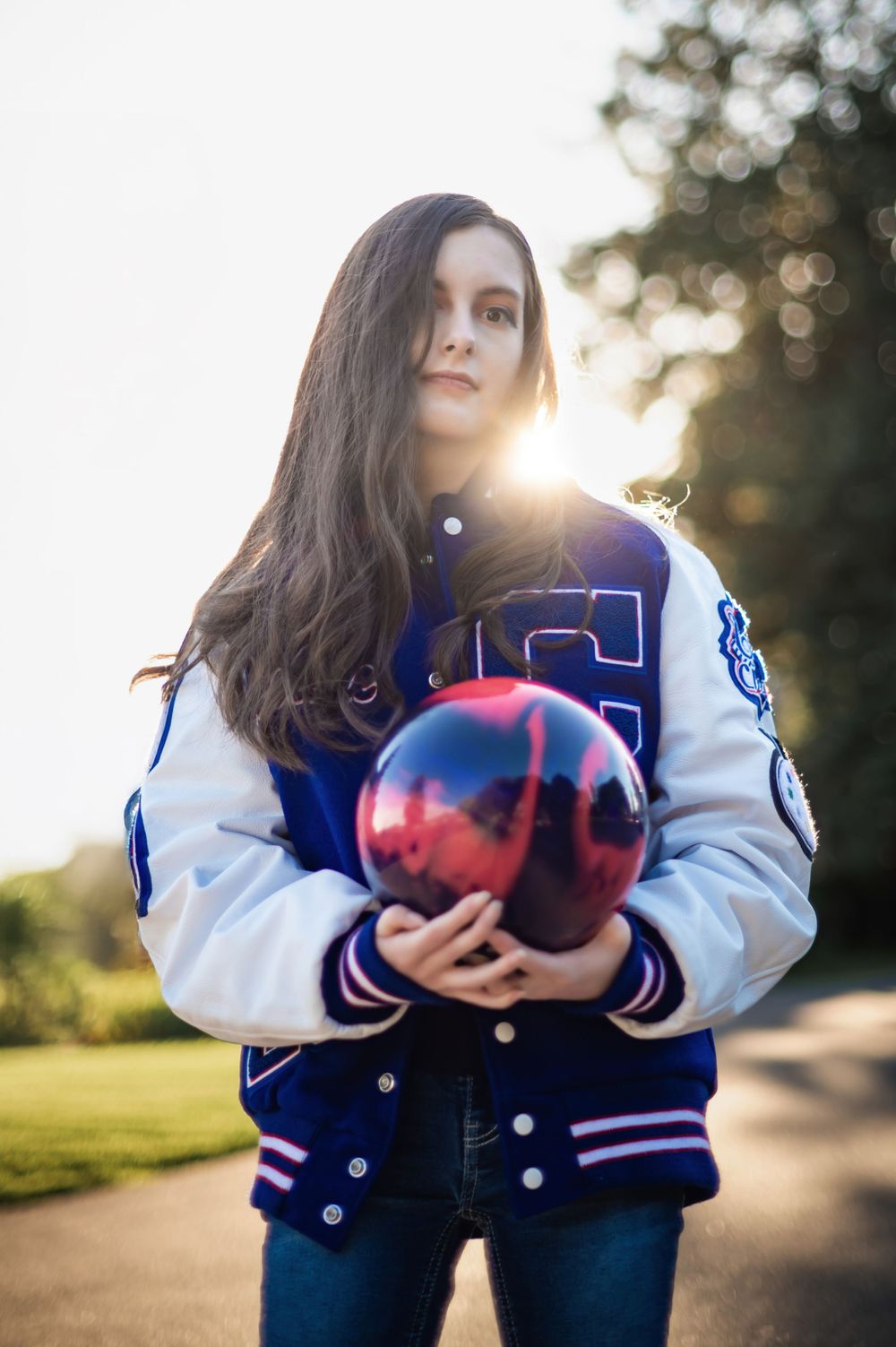 A high school senior portrait holding a bowling ball for her school sport in a letterman jacket in Hayden Idaho. By Jessica Rae Photography.