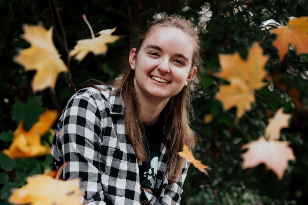 a high school senior sitting the grass with fall leaves falling all around her in spokane washington. By Jessica Rae Photography.