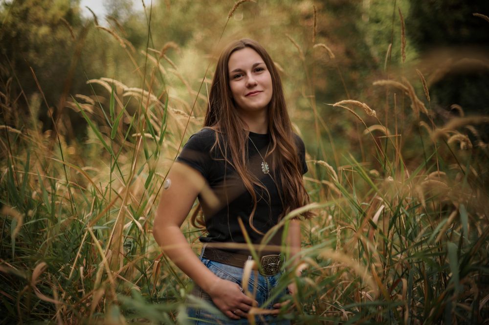 A high school senior posing for a portrait in a tall dreamy field during a senior portrait photo shoot. By Jessica Rae Photography.