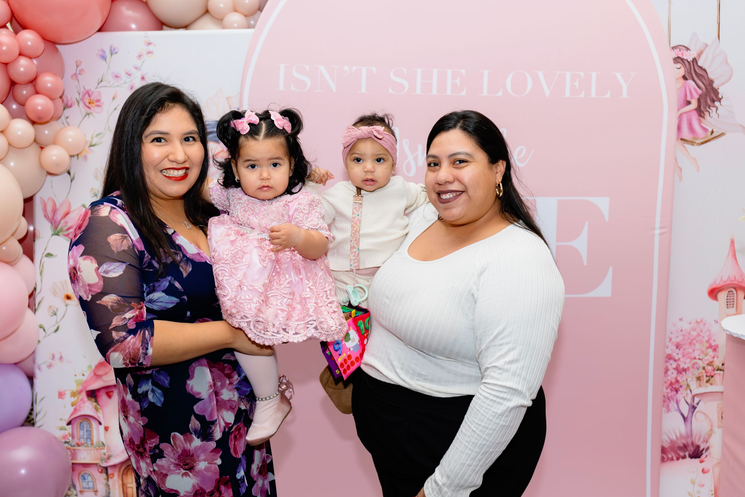 A family poses together at a pink birthday party with floral balloon decorations and blush colored backdrop.