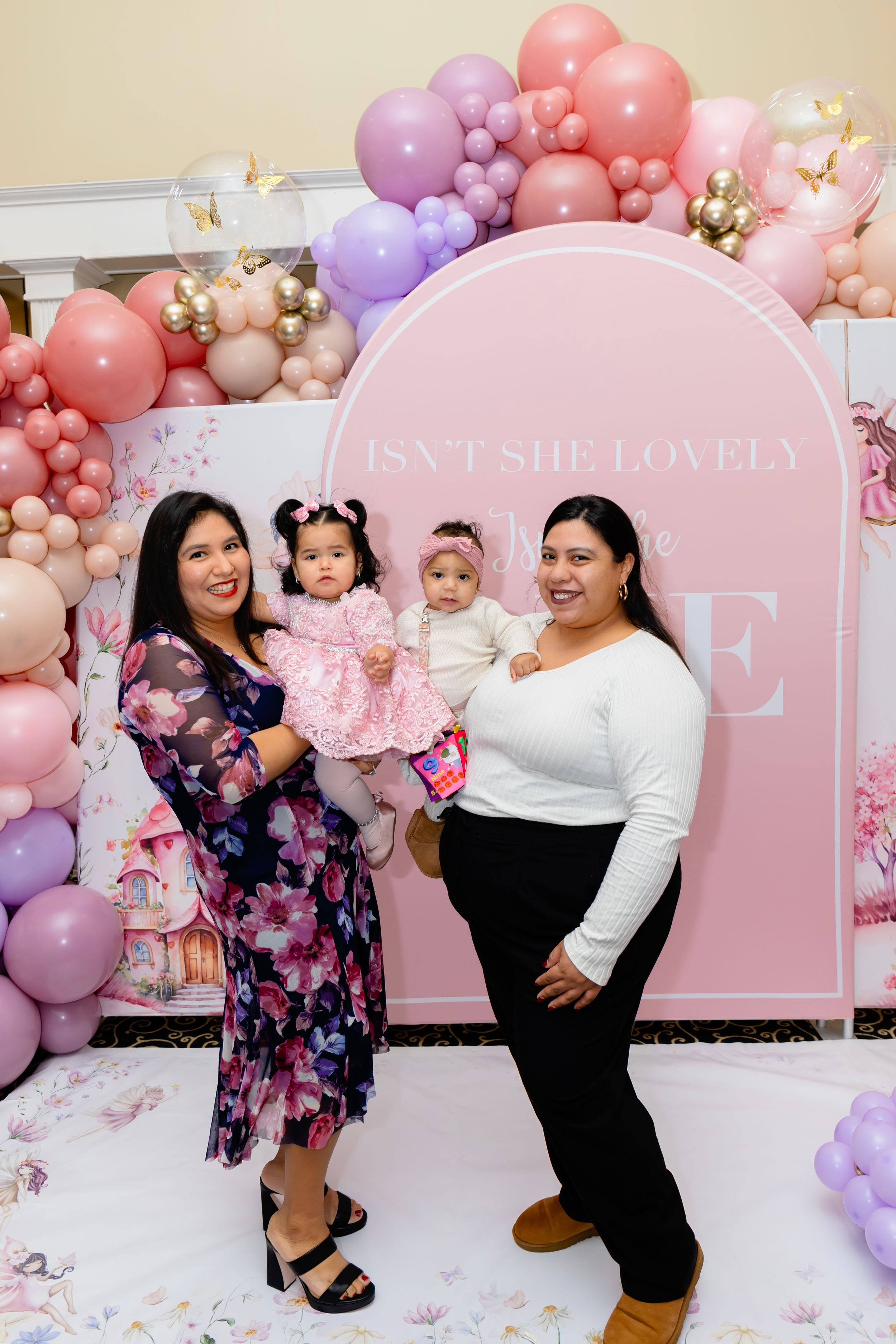 Festive party setup with pink archway backdrop and pastel balloon garland decorations in coral and lavender tones.
