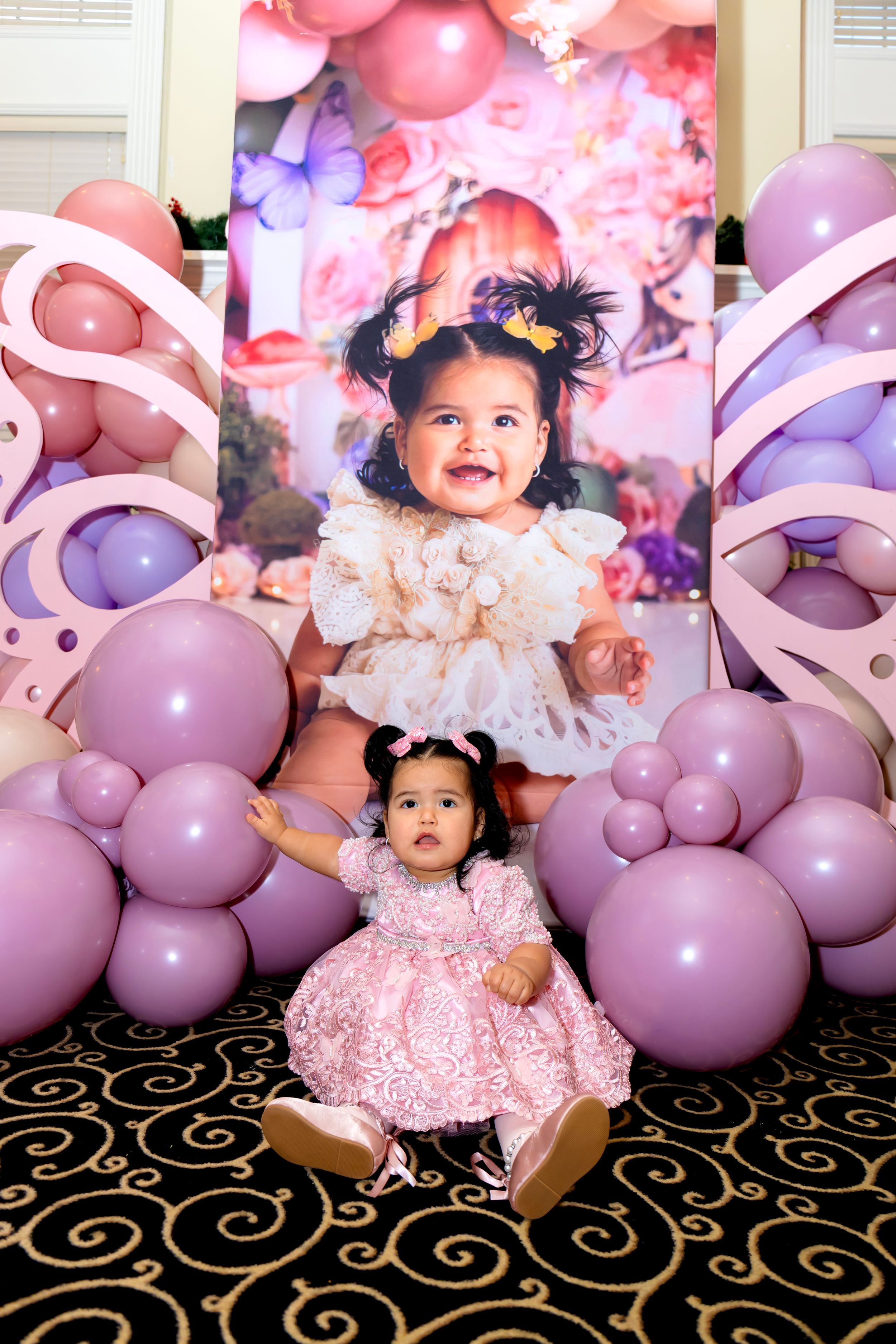 Pink and purple balloon display with dresses against patterned carpet and photo backdrop.