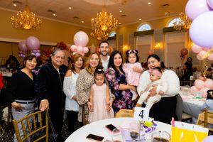 Group celebrates at an elegant event with pink and purple balloons under crystal chandeliers in a banquet hall.