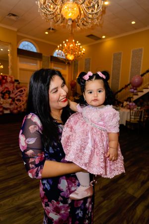 Elegant celebration in a ballroom with ornate chandeliers and hardwood floors, featuring formal pink and floral attire.
