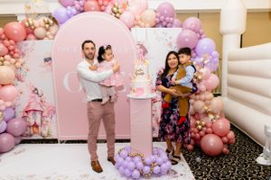 A festive pink and purple balloon arch decorates an indoor celebration space with elegant decor.