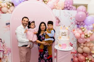Pink and purple balloon arch decorates a celebration with a pink cake and floral backdrop.