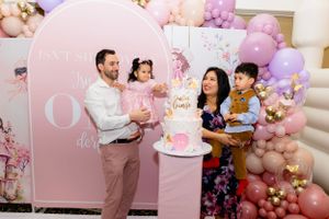 Elegant pink and white first birthday party setup with balloon arch decorations and a pink arch backdrop around a cake table.