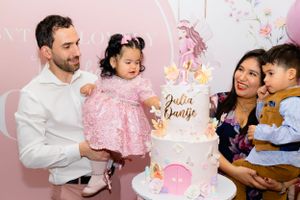 Group gathered around elegant white and pink birthday cake with unicorn topper at a pink themed party celebration.