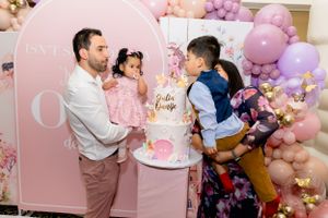 Pink celebration setup features an arched backdrop, balloon decorations, and cake display table.