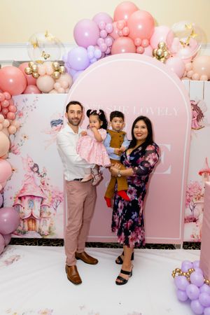 A party backdrop with pink and purple balloon garland arch decorations against a whimsical fairy garden theme design.