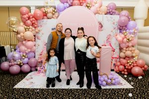 A group poses in front of a pink and purple balloon arch with a round backdrop at a festive celebration.