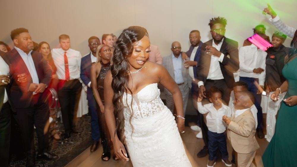 Wedding reception dance party with bride in white strapless gown dancing surrounded by guests on dance floor.