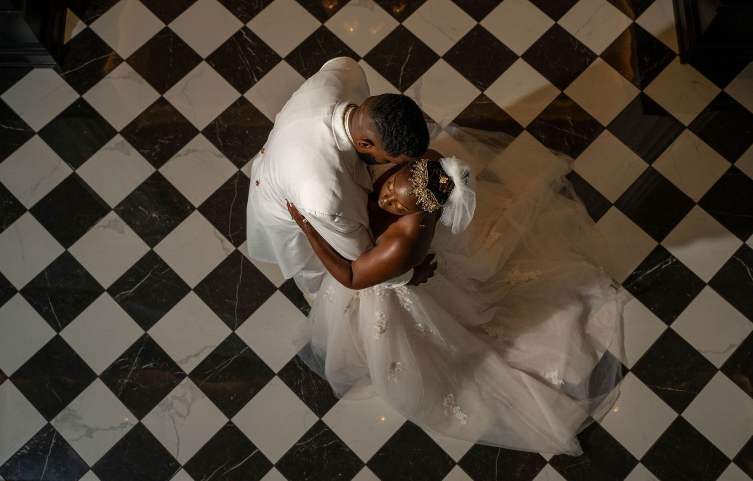 Overhead view of couple dancing on black and white checkered floor during wedding celebration.