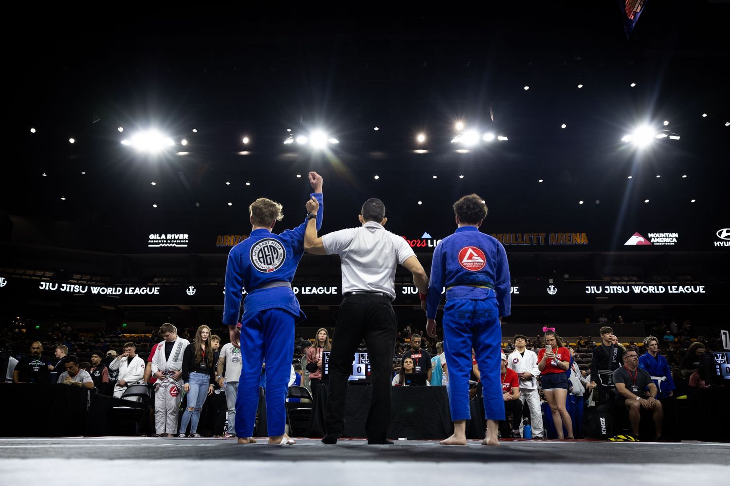 Competitors lined up at a martial arts tournament with bright overhead lighting. Winner has his arm raised