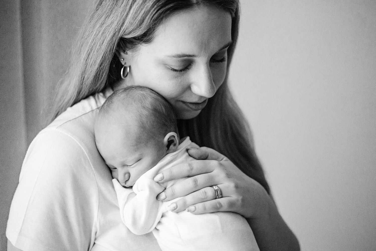 Black and white portrait of a tender moment as a mother in white clothing holds and comforts her sleeping baby.