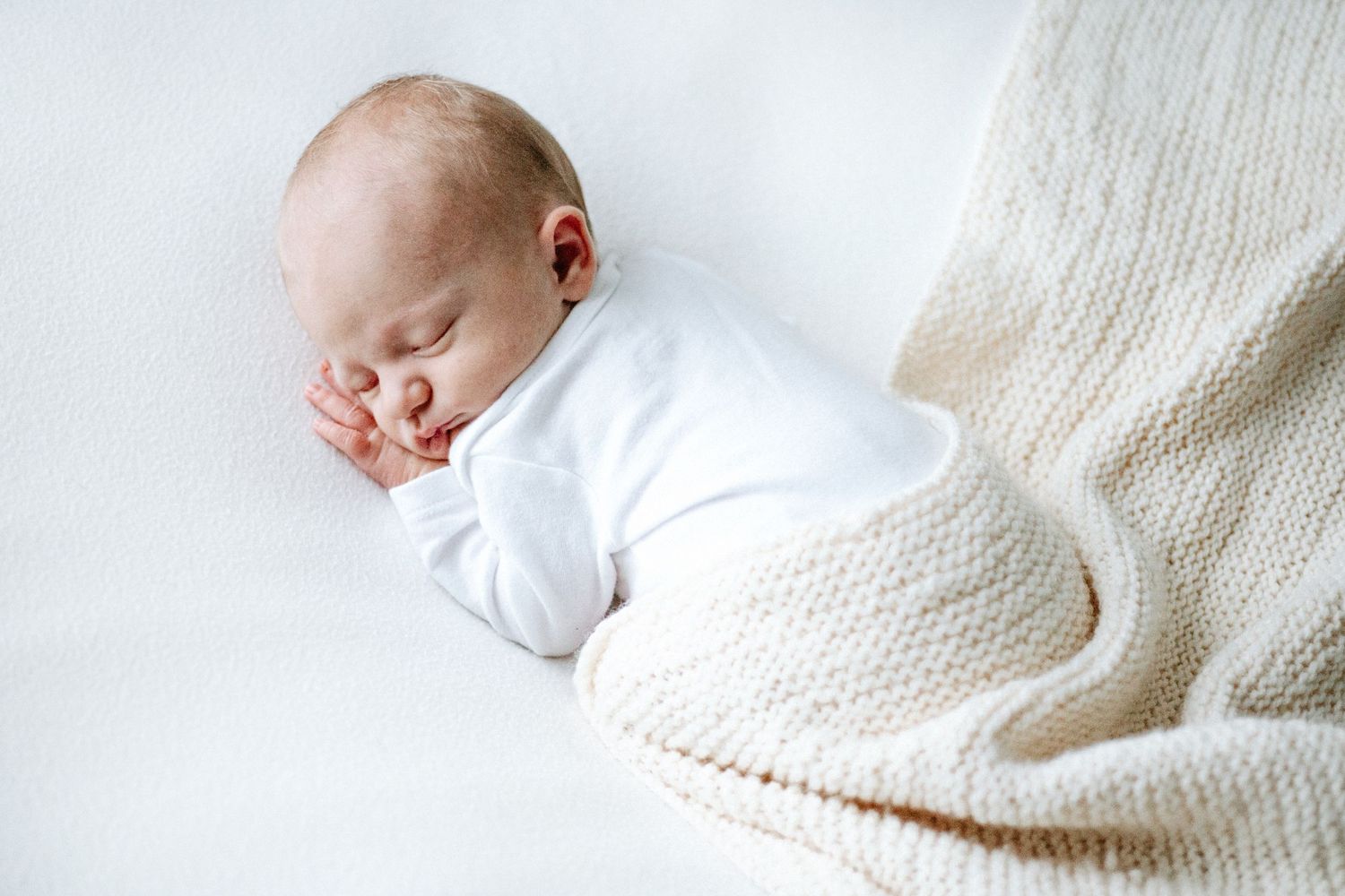 A sleeping newborn wrapped in a cosy white knit blanket rests peacefully against a light background at a newborn photoshoot in nottingham