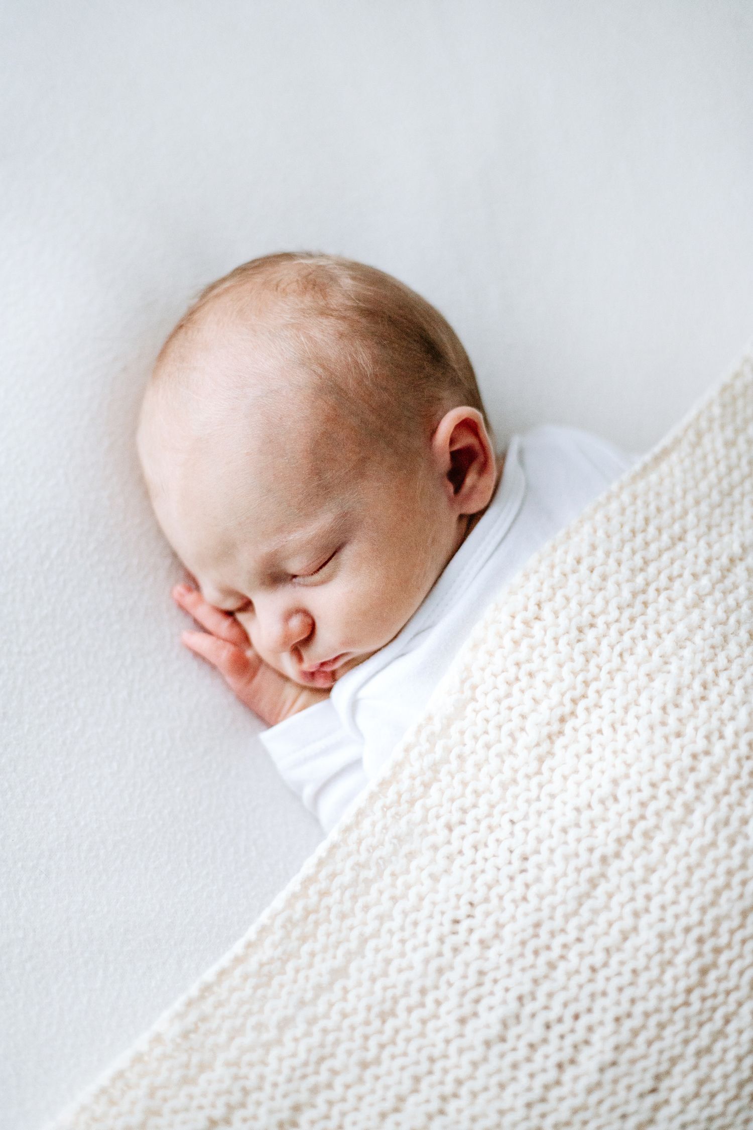 A peaceful sleeping baby rests on a white blanket with a textured knit pattern.
