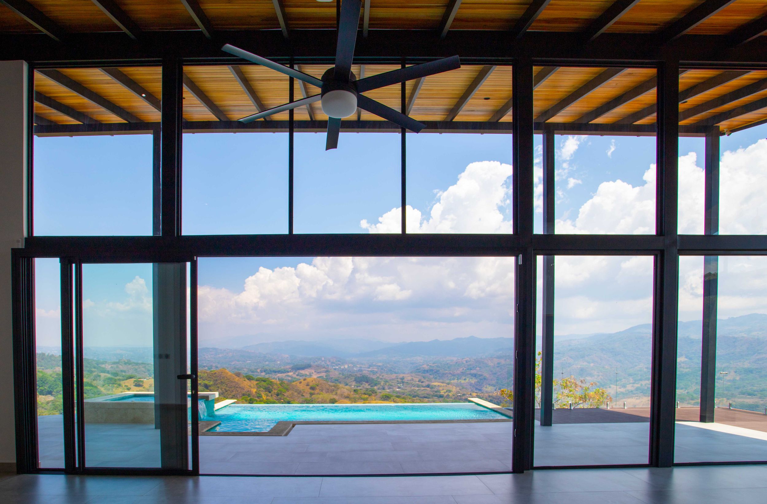 Open living area in Atenas, Costa Rica, with floor-to-ceiling glass windows showcasing expansive views of the countryside and distant mounta