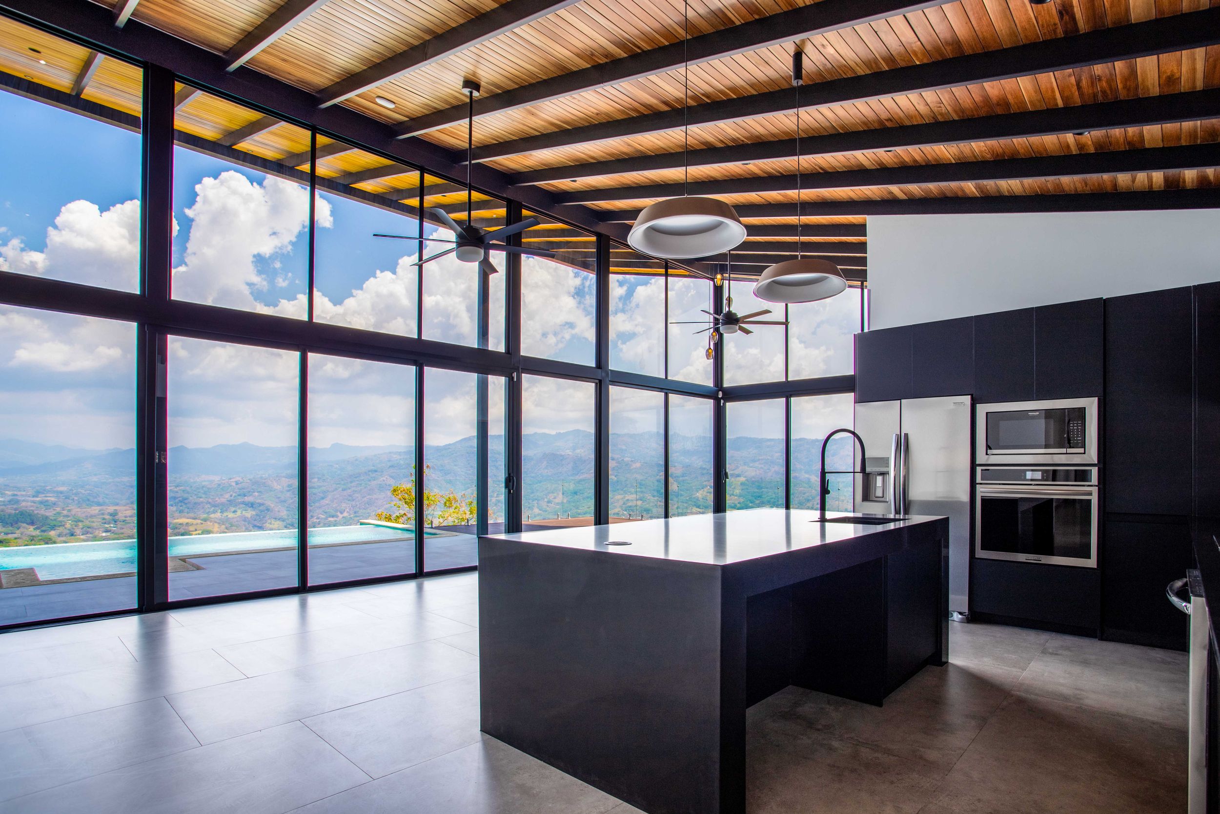 Modern kitchen in a luxury home in Atenas, Costa Rica, featuring sleek black countertops and large windows offering panoramic views of the l