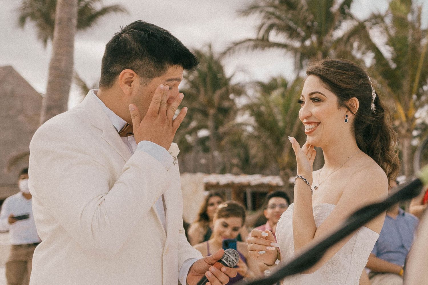 A tropical beach wedding ceremony with palm trees swaying in the background.