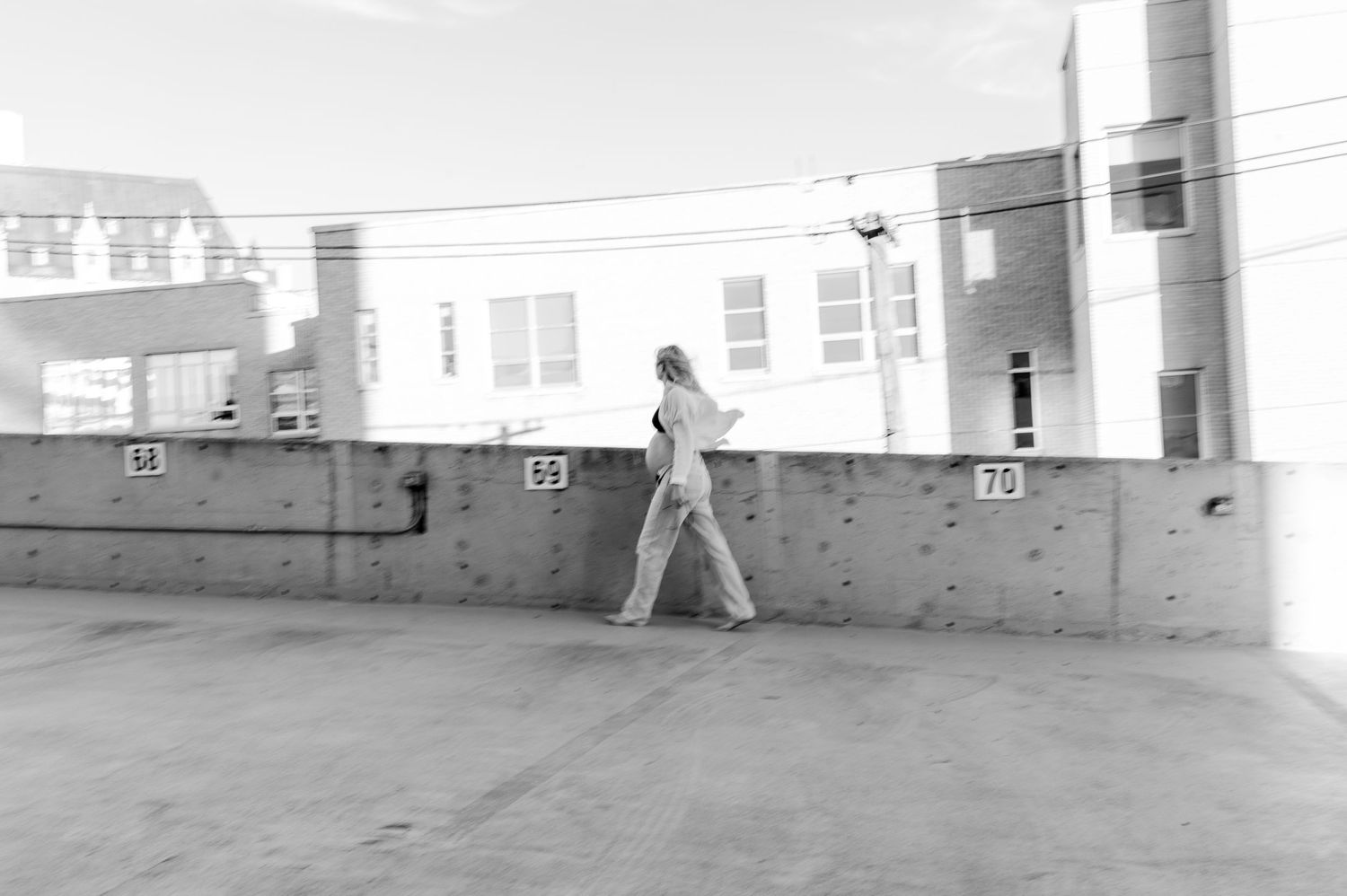 A black and white photograph of someone walking along an urban concrete barrier.