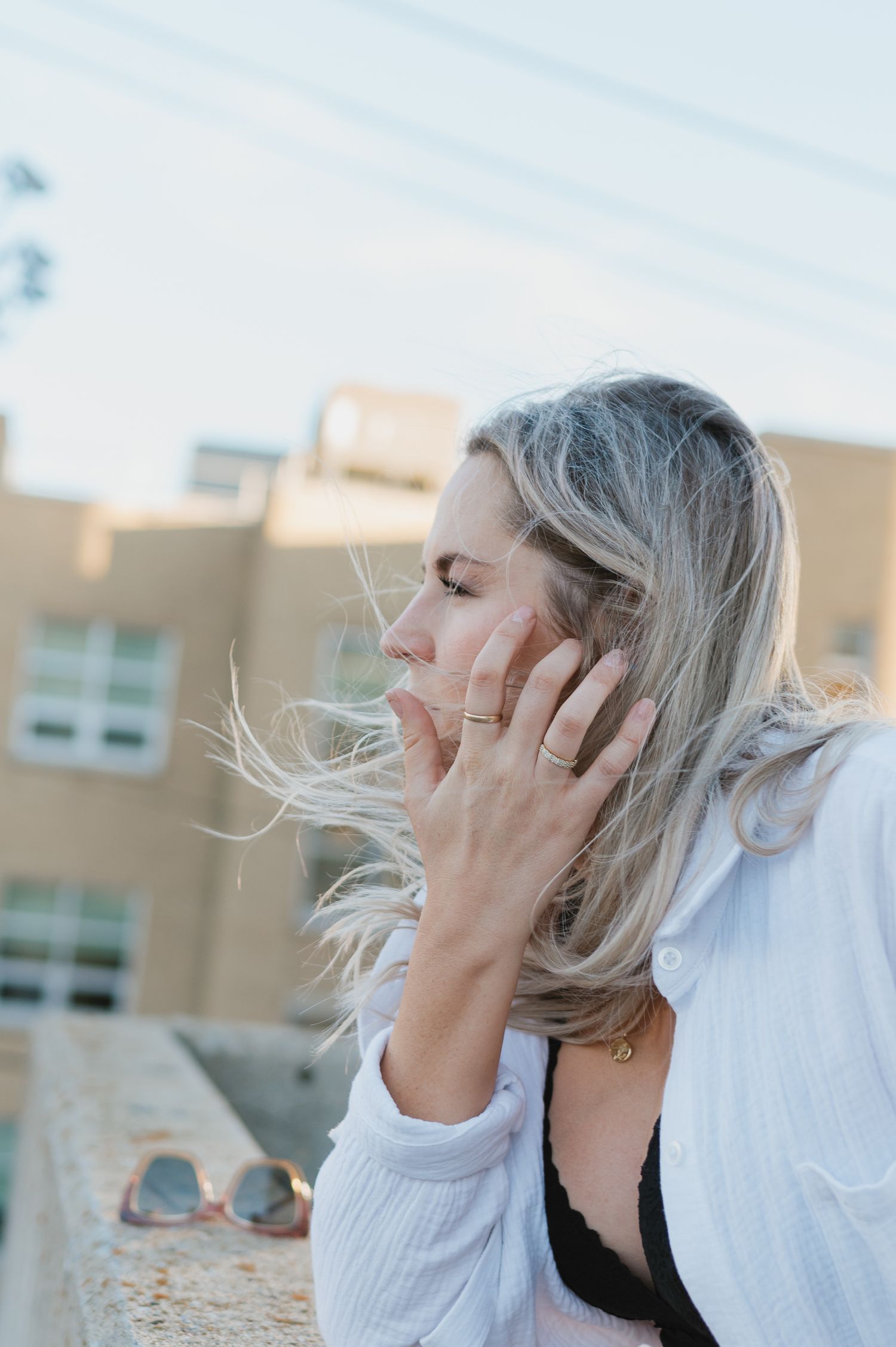 A candid outdoor portrait with wind-blown hair against an urban backdrop.