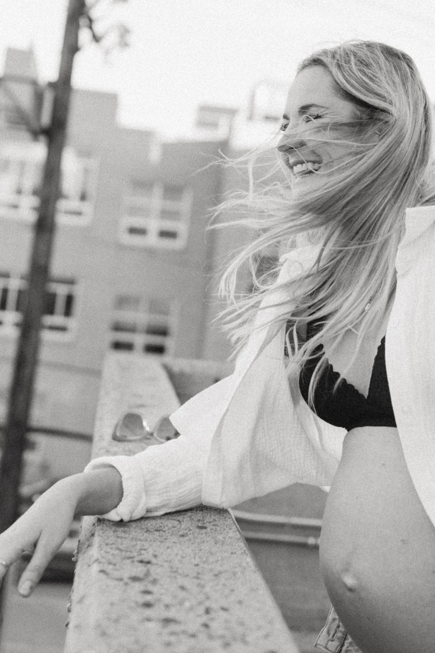 A joyful maternity photoshoot on an urban rooftop with wind-swept hair and a white button-down shirt.