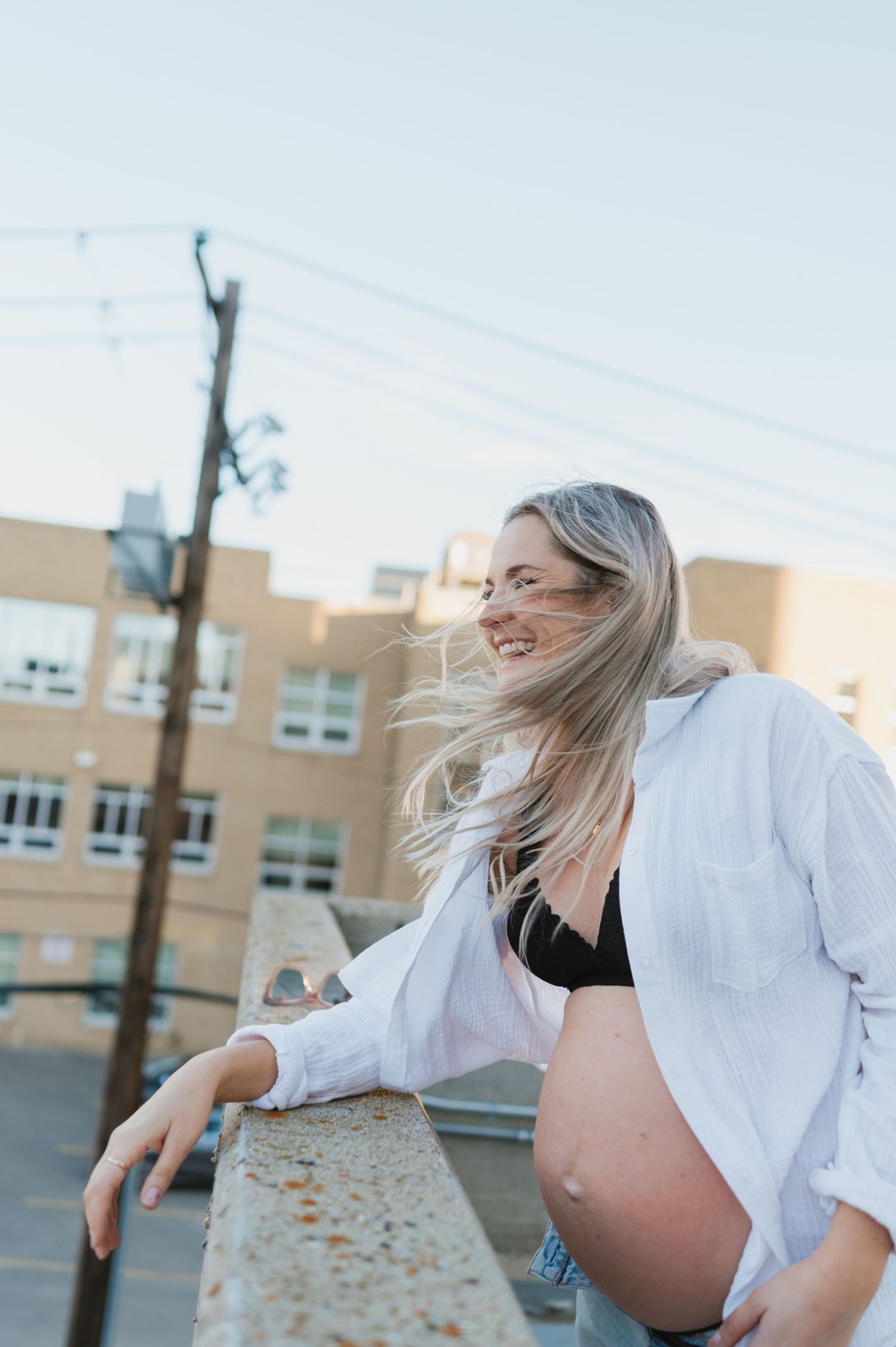 A joyful maternity photo with flowing hair and white shirt against urban architecture.