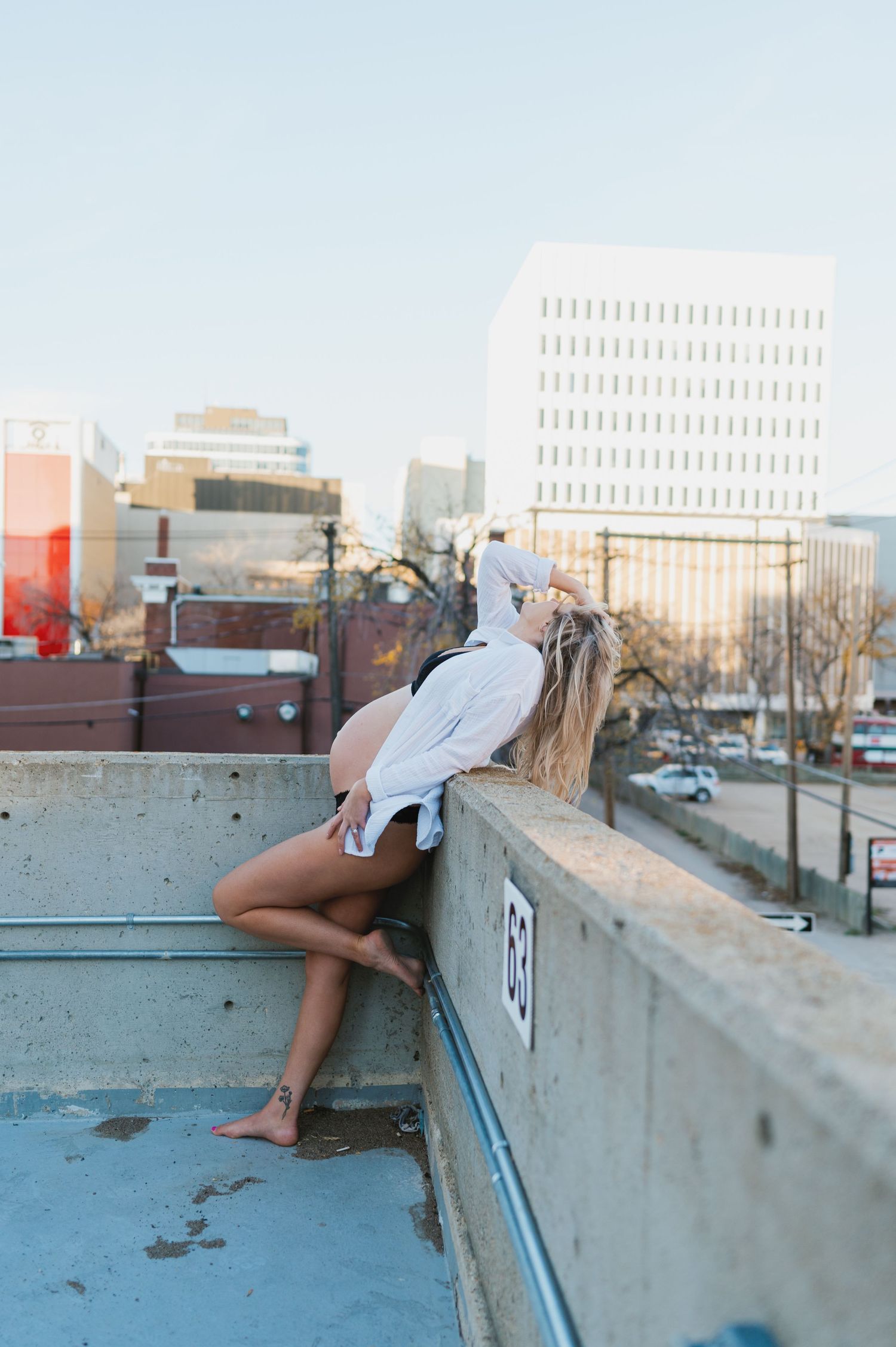 Artistic maternity photo featuring a flowing white shirt against an urban cityscape backdrop.