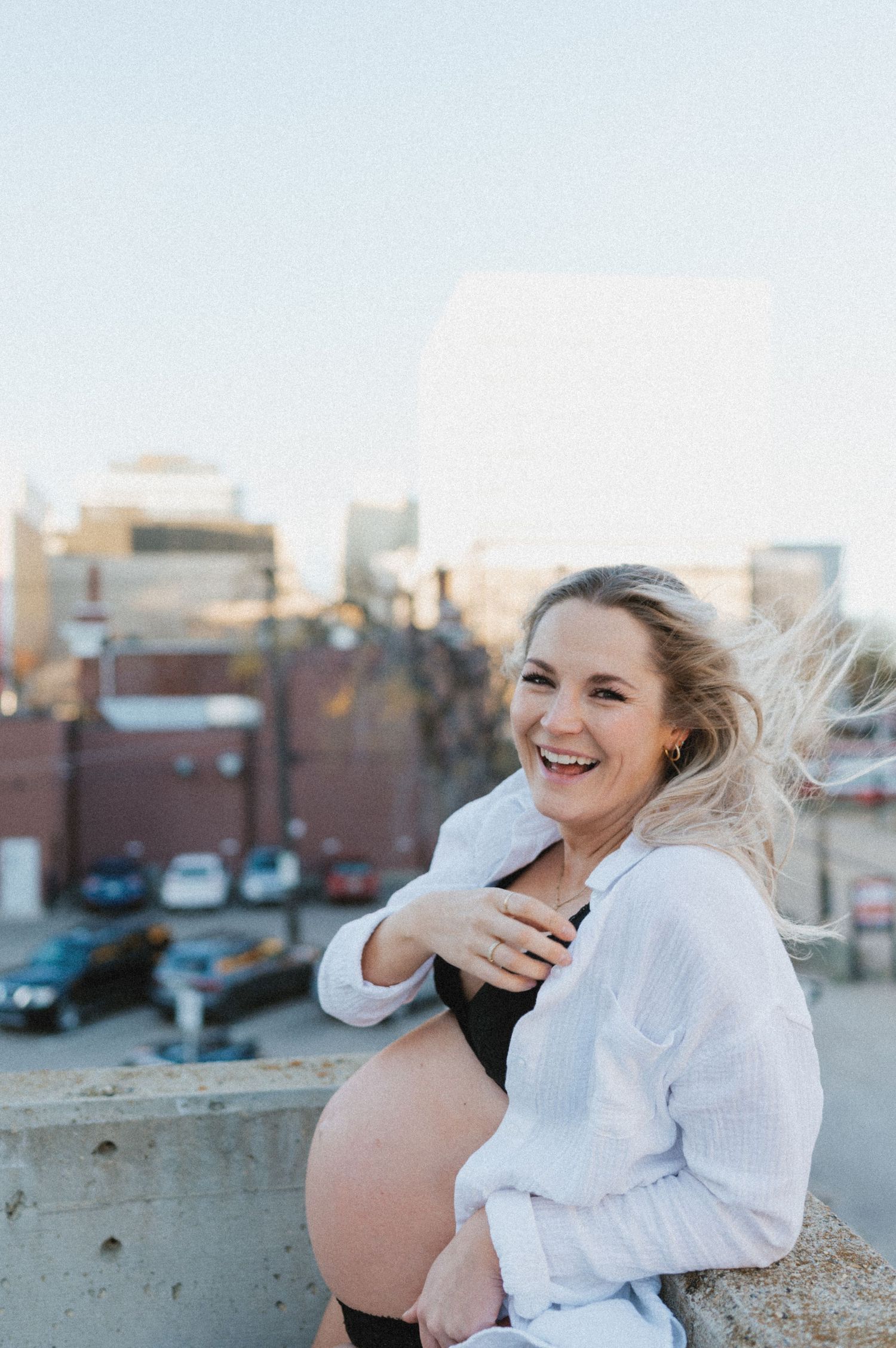 Candid pregnancy photo showing pure joy while posing on a city rooftop at sunset.