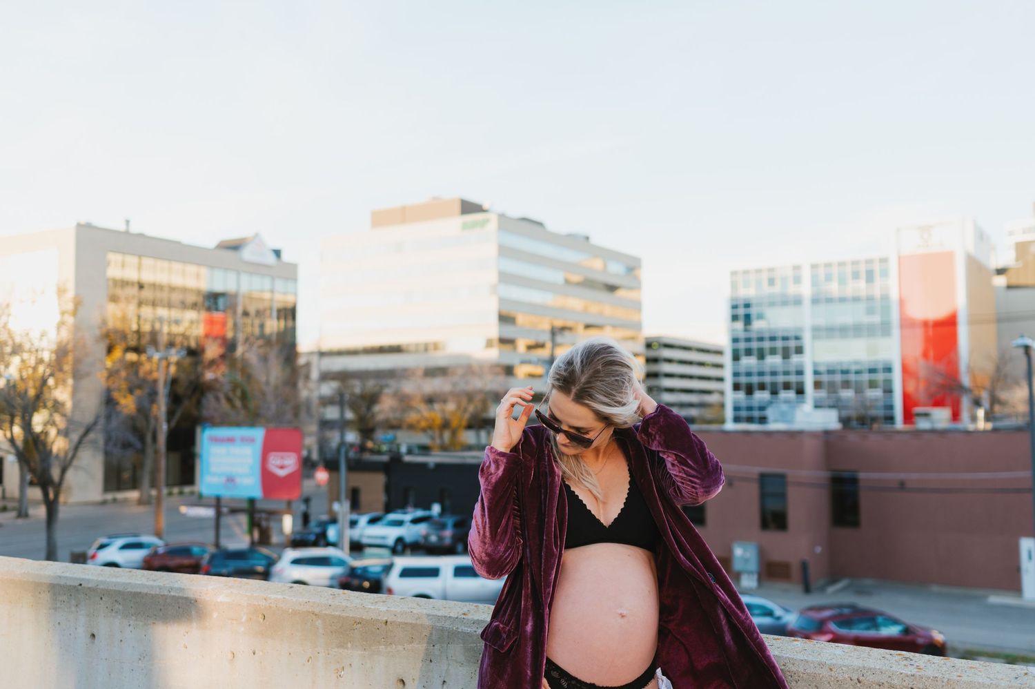 Maternity photo featuring a burgundy cardigan against urban architecture at golden hour.