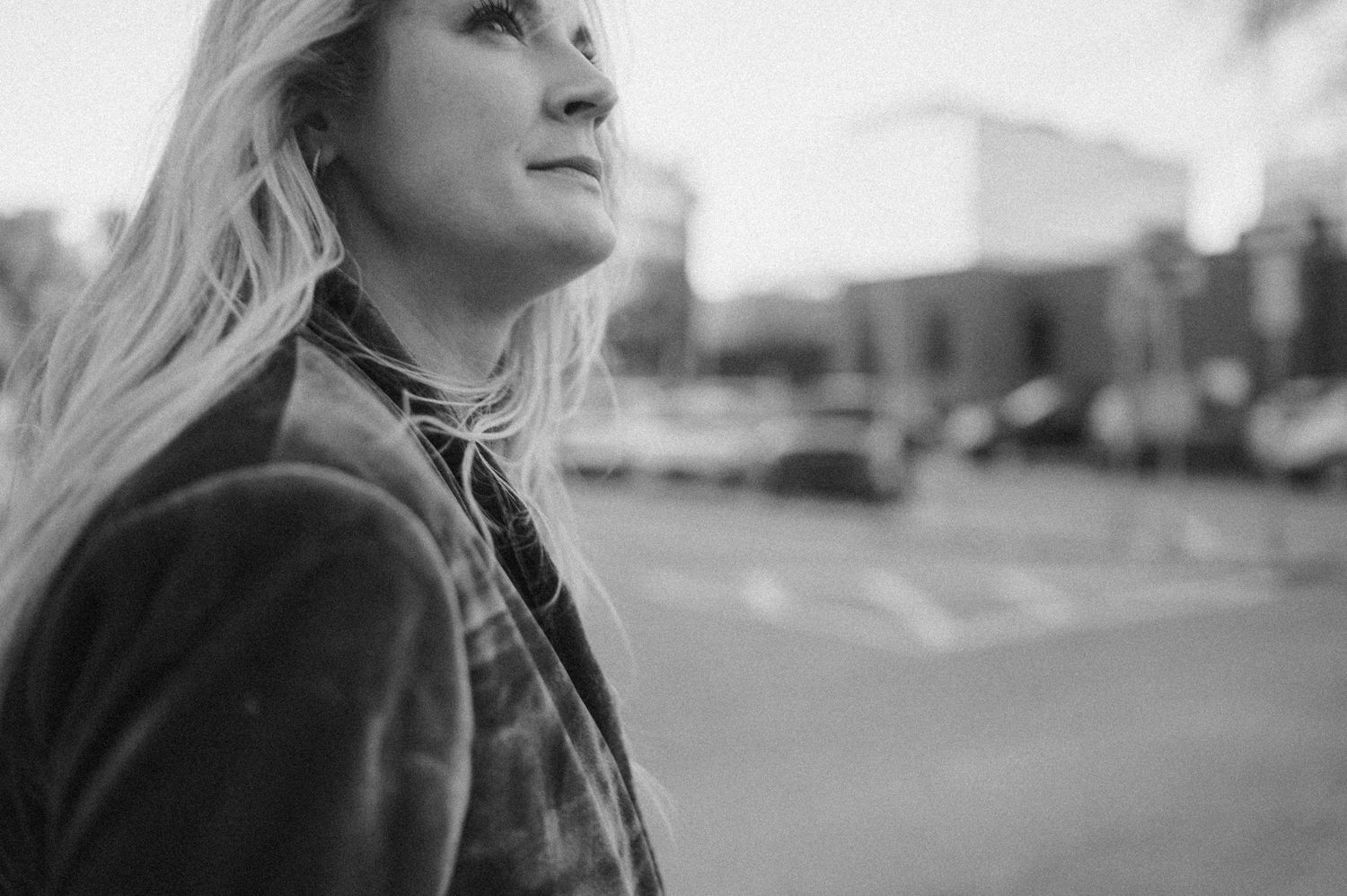 Black and white profile portrait with wind-swept hair against an urban backdrop.
