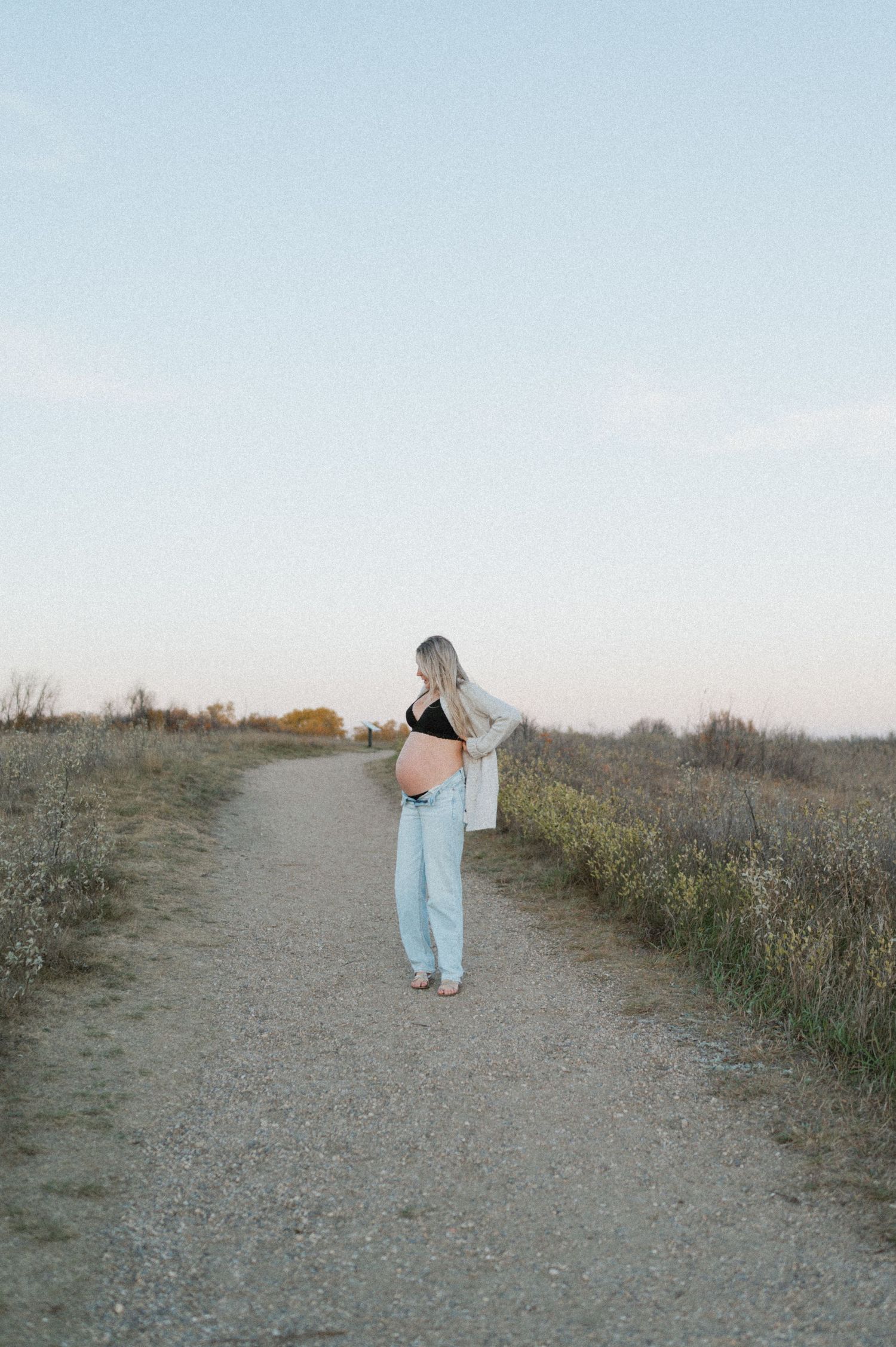 Serene maternity photo on a rural path during golden hour.