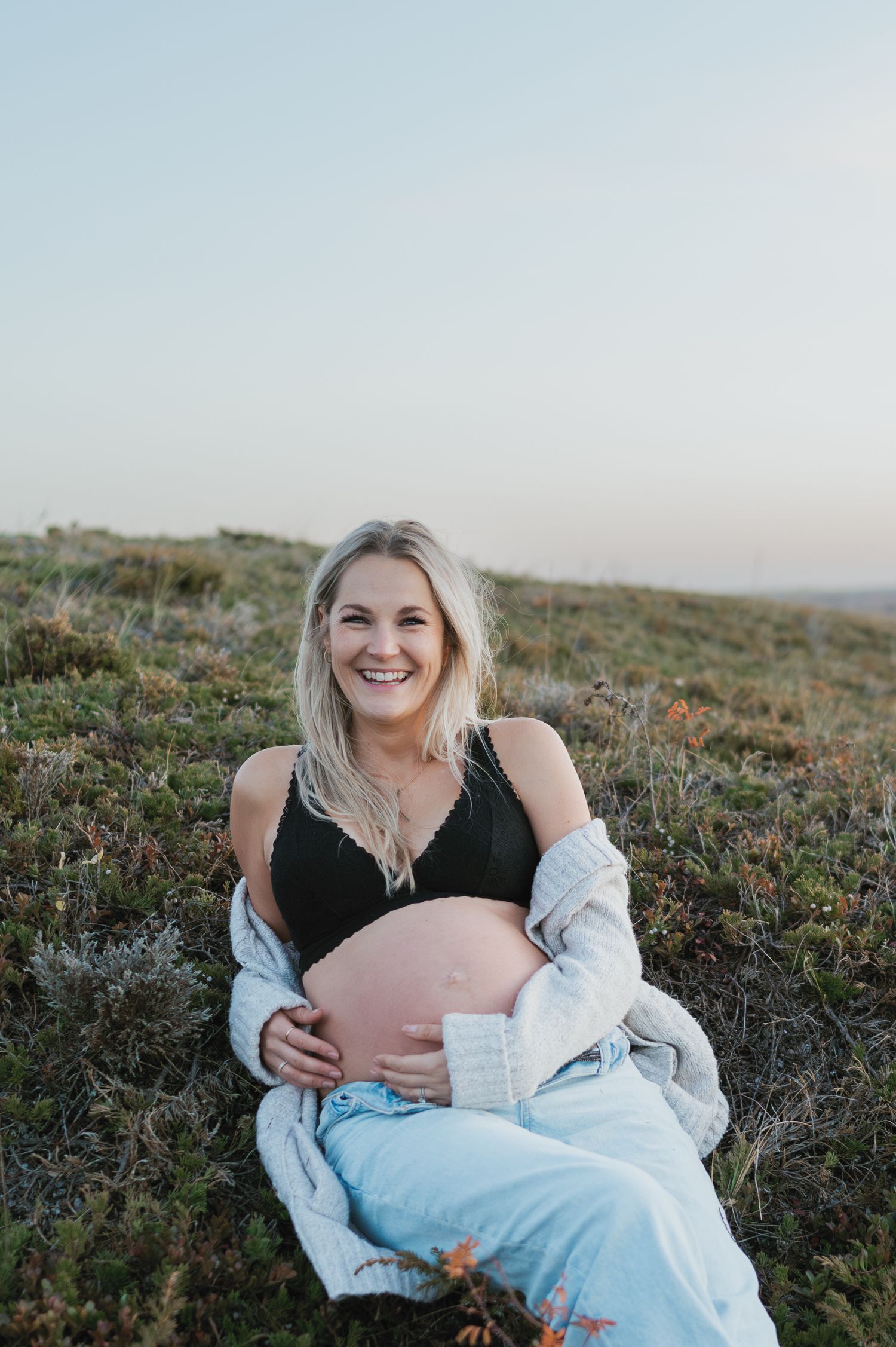 A joyful maternity portrait taken outdoors with natural lighting and scenic background.