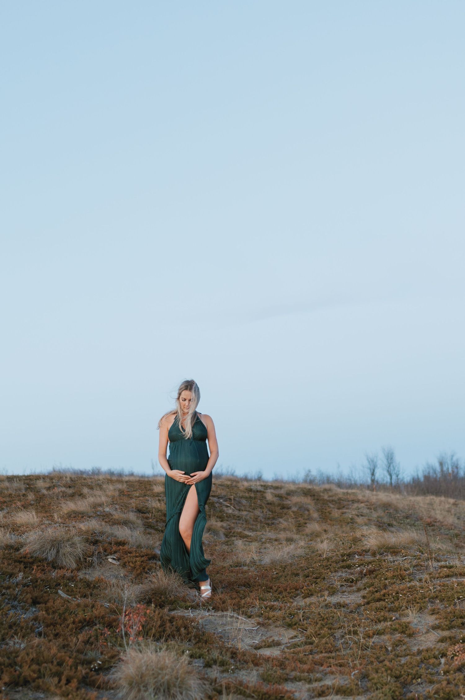 Woman in green dress poses on hillside during sunset photo session.