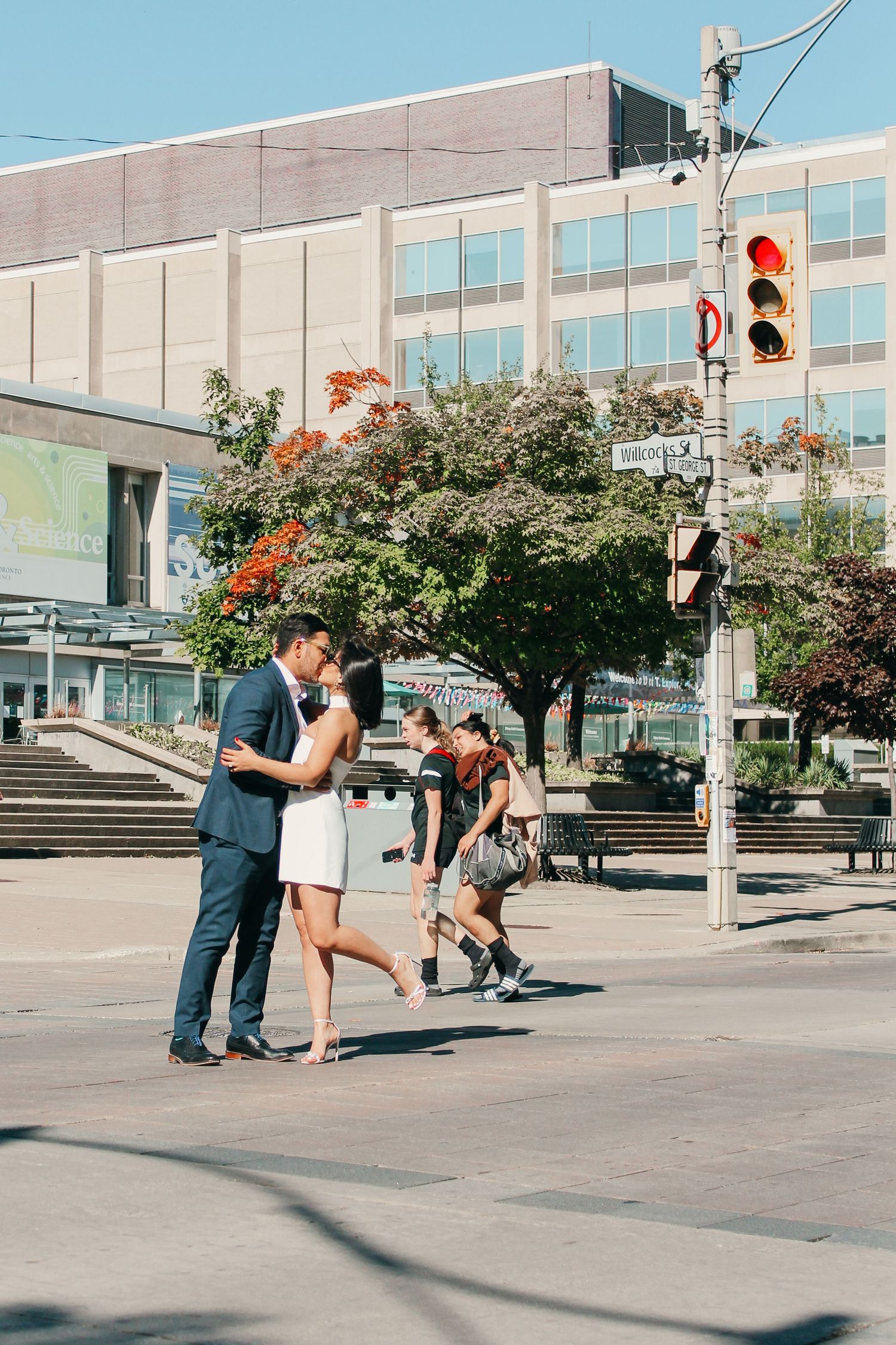 Couple sharing an intimate moment on a busy city street corner with traffic lights and urban architecture.