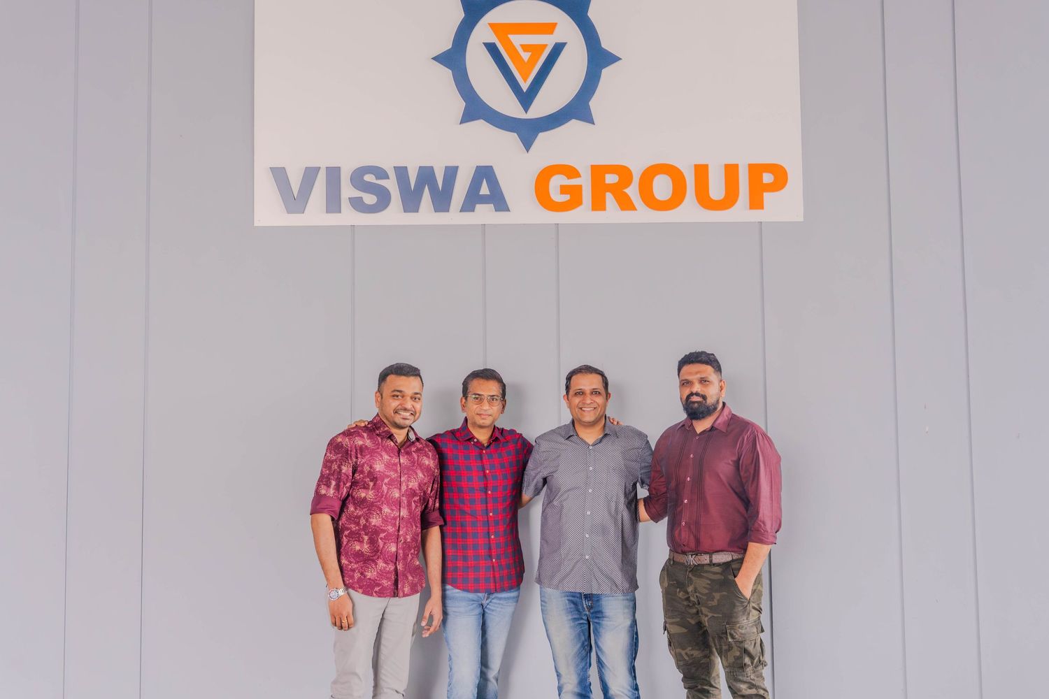 Four staff members standing against a wall with the Viswa Group company logo.