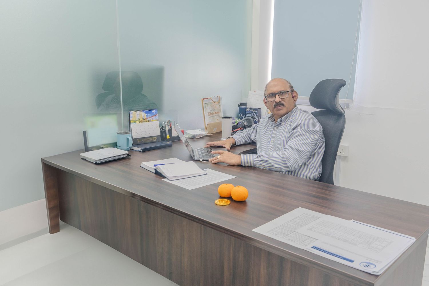 Executive working at large wooden desk in bright modern office setting.