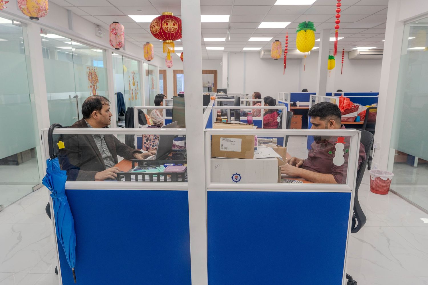 Modern office workspace with cubicles decorated with colorful lanterns and lighting.