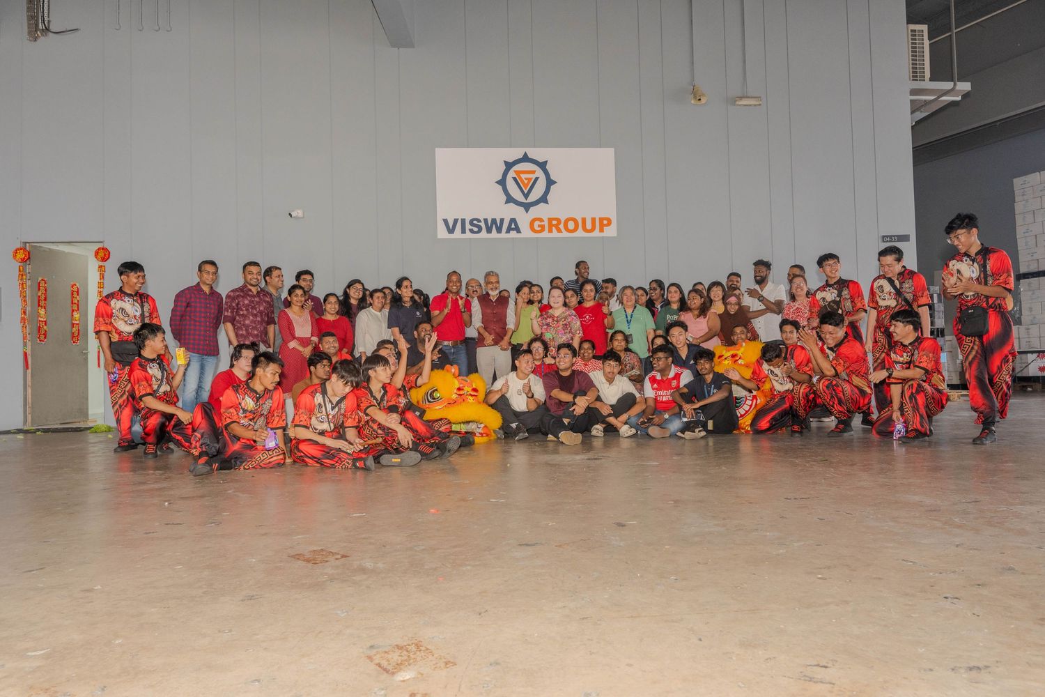 Large group photo of employees in red attire with lion dance performers at company event.