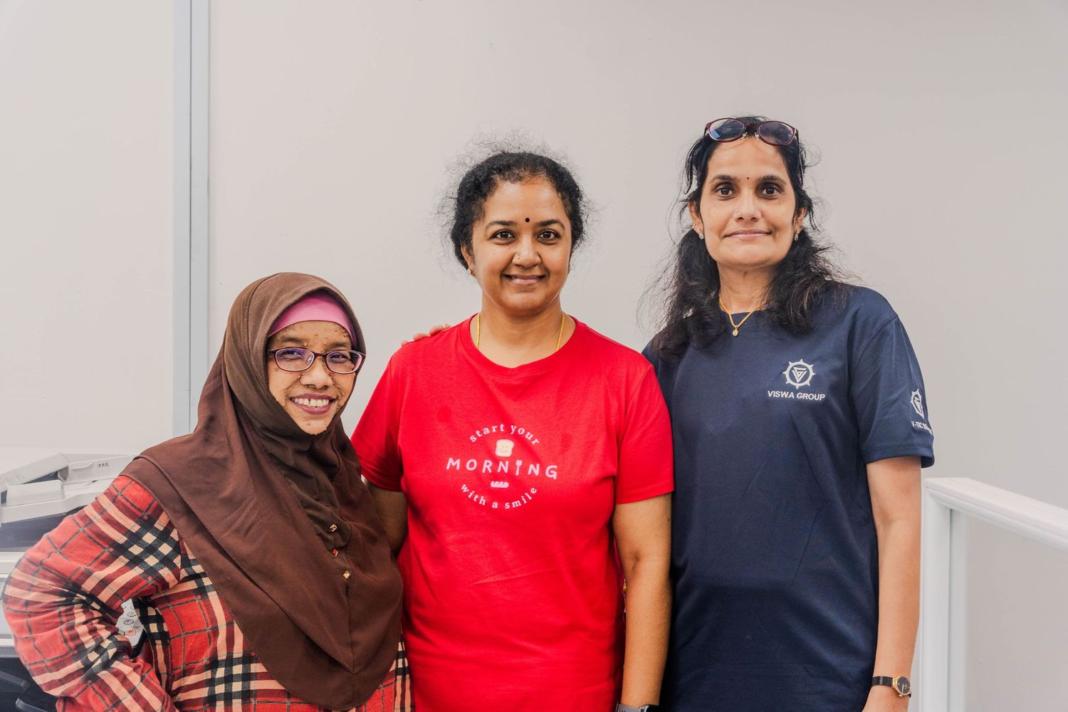 Three staff members in office attire standing together in front of a white wall.
