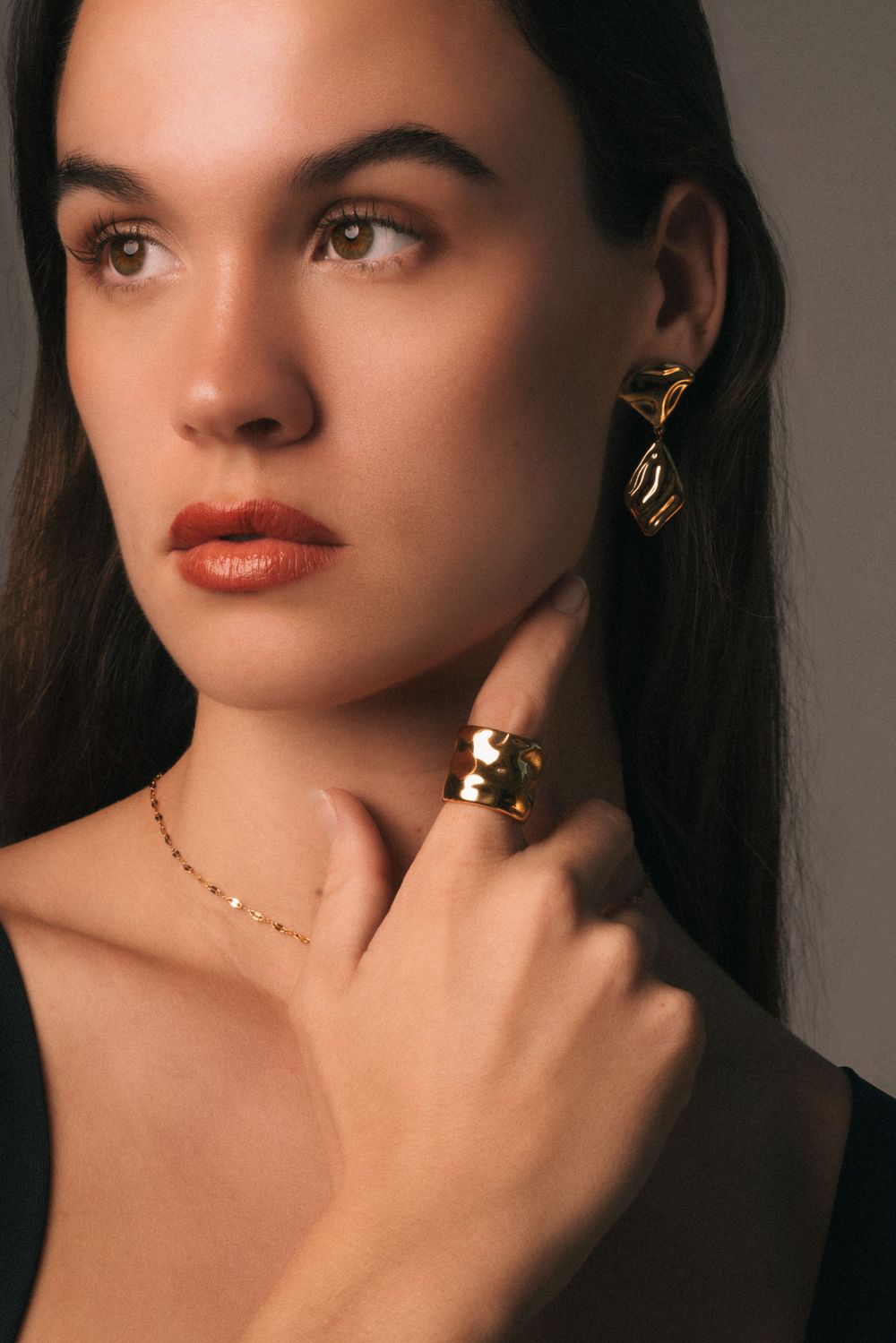 Dramatic portrait featuring delicate jewelry and natural makeup in warm lighting.