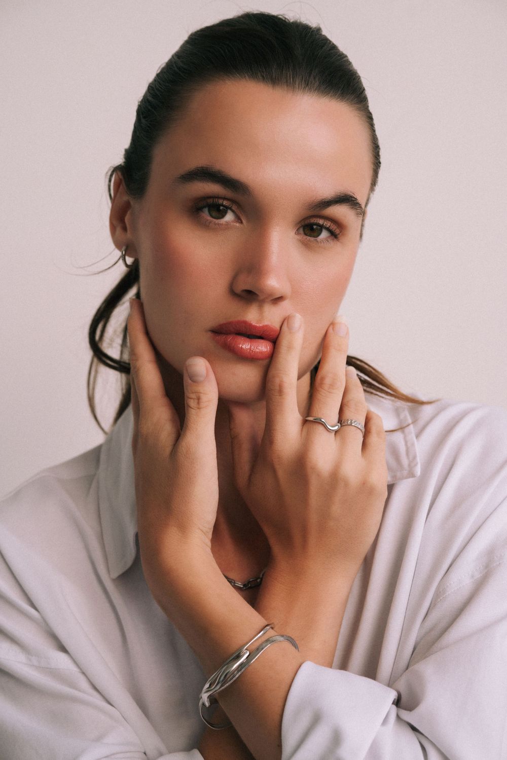 Beauty portrait highlighting delicate jewelry and natural makeup against light background.