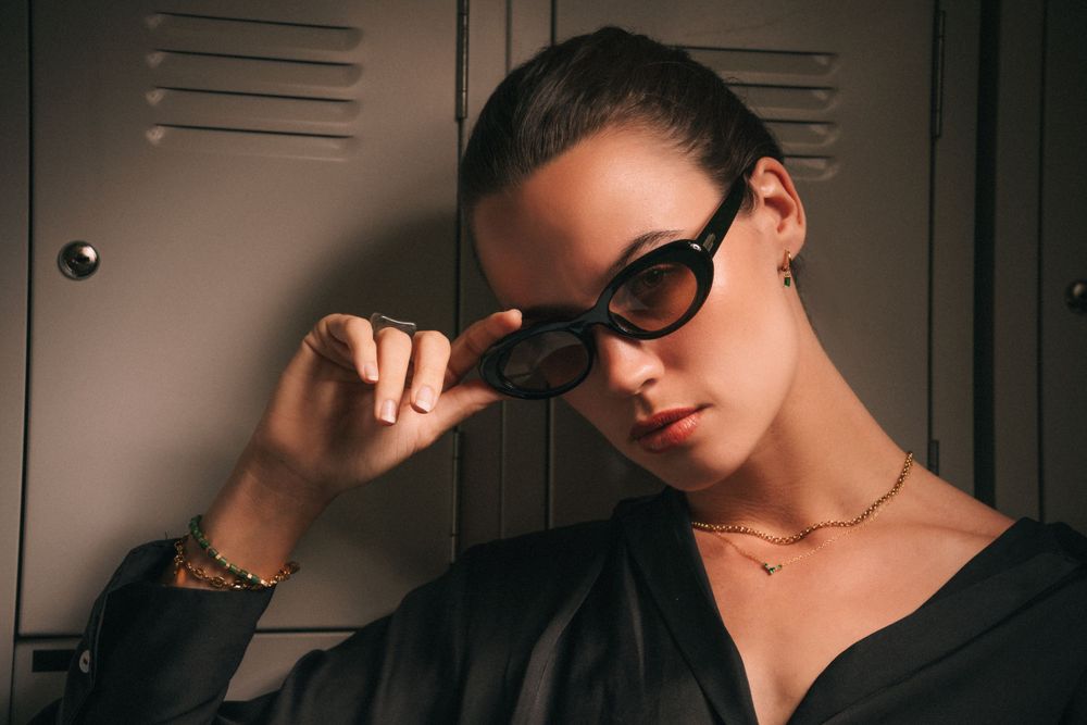 Fashion portrait with sunglasses and gold jewelry against dark locker background.